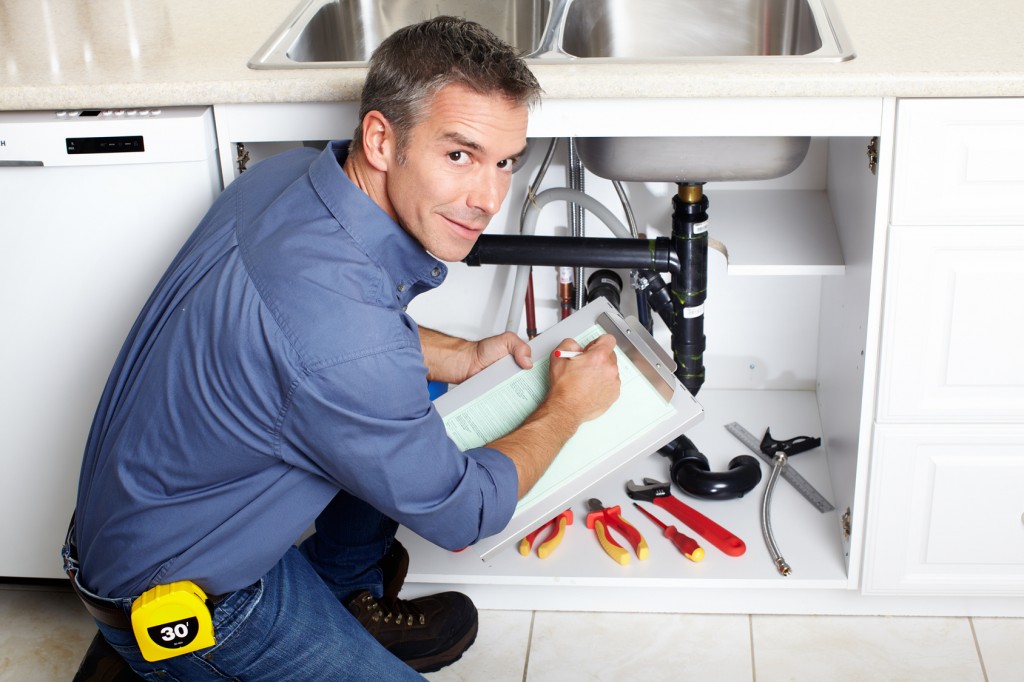 Young smiling plumber fixing a sink in the kitchen.